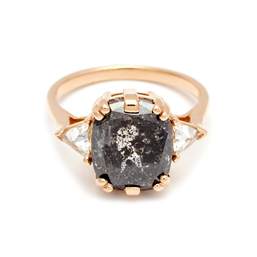 A three stone engagement ring with a cushion cut grey diamond center stone with two white diamond trillion side stones set in yellow gold.