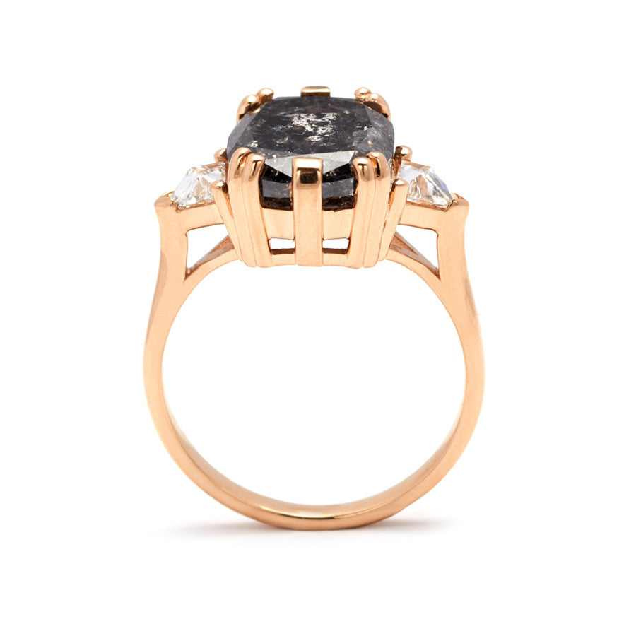 A side view of a three stone engagement ring with a cushion cut grey diamond center stone with two white diamond trillion side stones set in yellow gold.