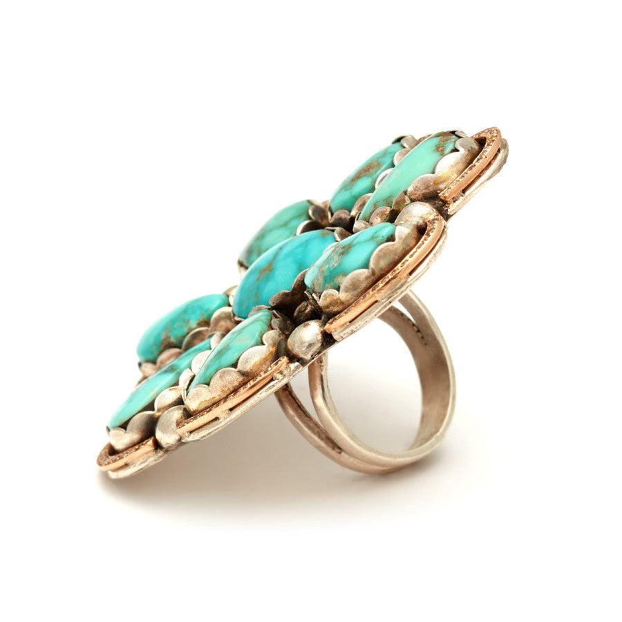 Angled view of a flower shaped ring with turquoise stones and white diamond halo set in sterling silver and yellow gold.