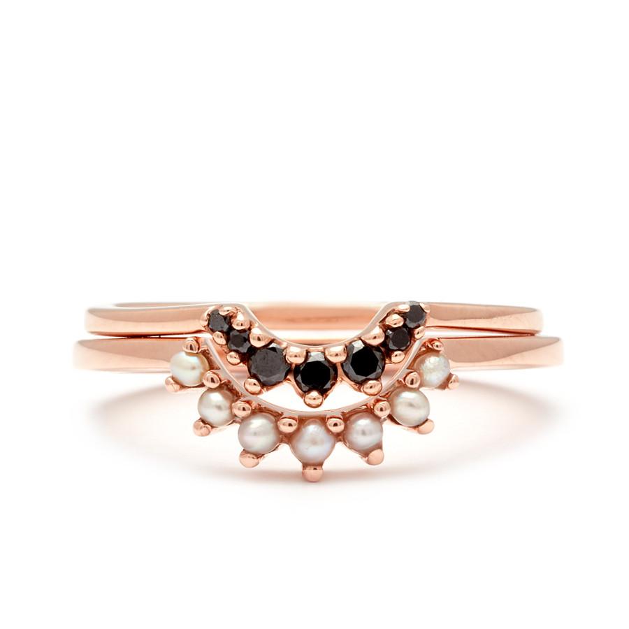 Two curved bands set in rose gold, one with smaller black diamonds and one with slightly larger pearls.