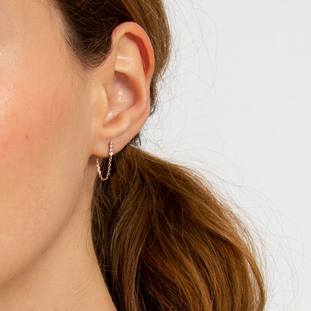 A single earring with four white diamonds with a chain connecting to the ear back set in yellow gold on a light-complexion ear., White Gold, Rose Gold, Yellow Gold