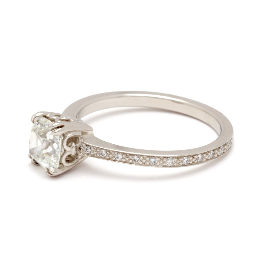 Angled view of a solitaire ring with a knife edge white diamond with white diamond pave on either side set in white gold.