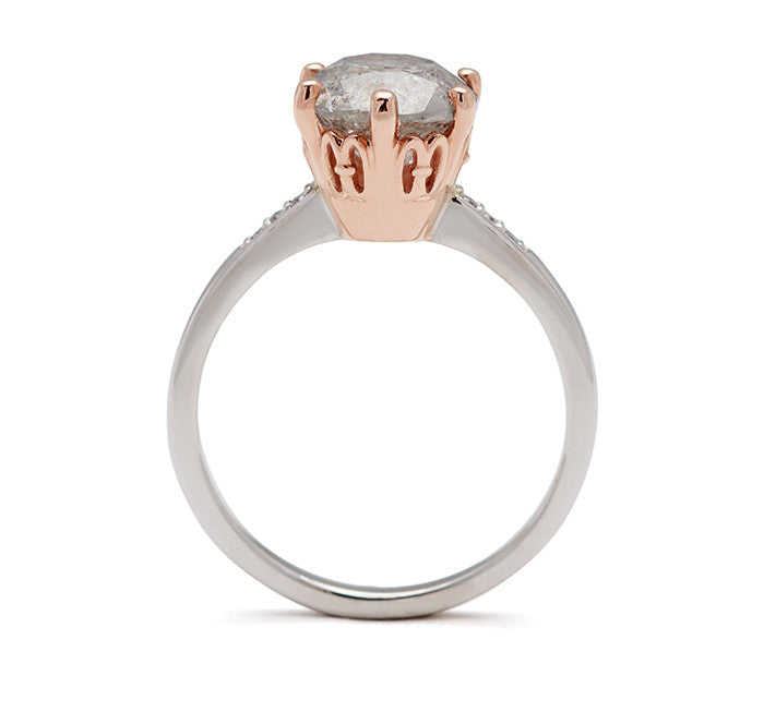 Side view of a solitaire ring with a round grey diamond with white diamond pave on either side set in a rose gold basket and a white gold band.