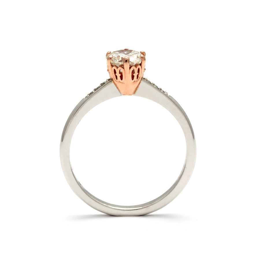 Side view of a solitaire ring with a round shape white diamond with white diamond pave on either side set in a rose gold basket and white gold band.