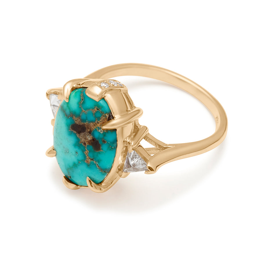 Angled view of a three stone engagement ring with an oval shaped turquoise center stone with claw prongs two white diamond trillion side stones set in yellow gold.