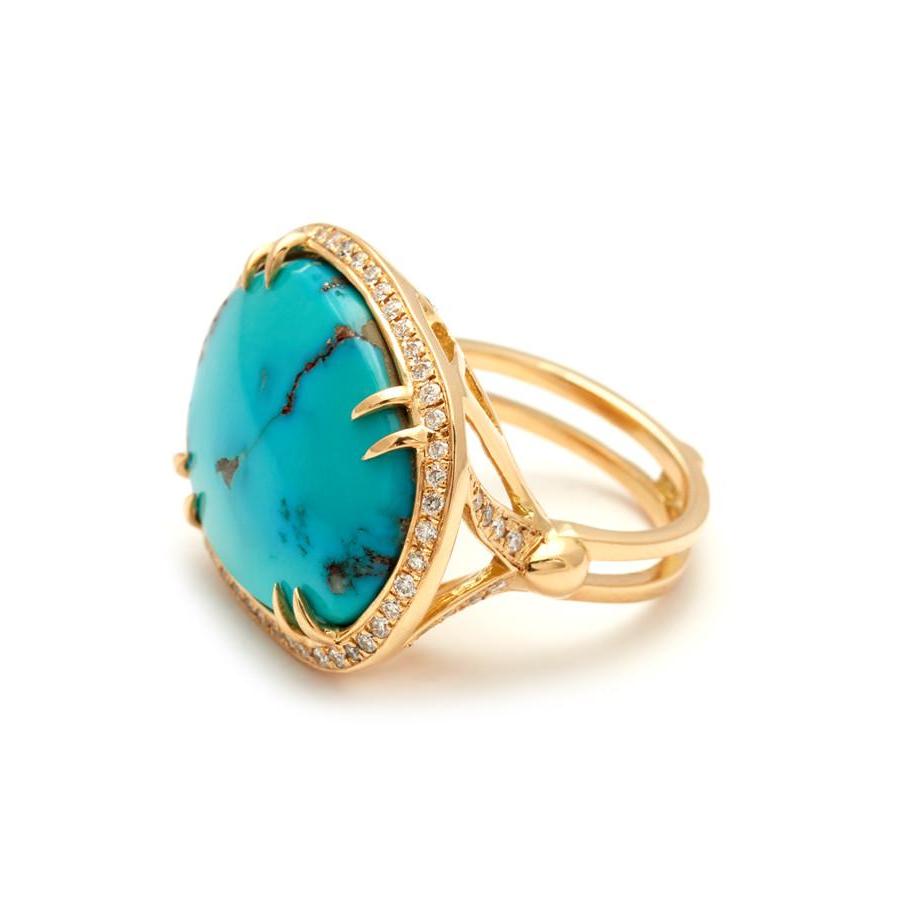 Angled view of an oval shape turquoise center stone with double claw prongs surrounded by a white diamond pave halo set in yellow gold.