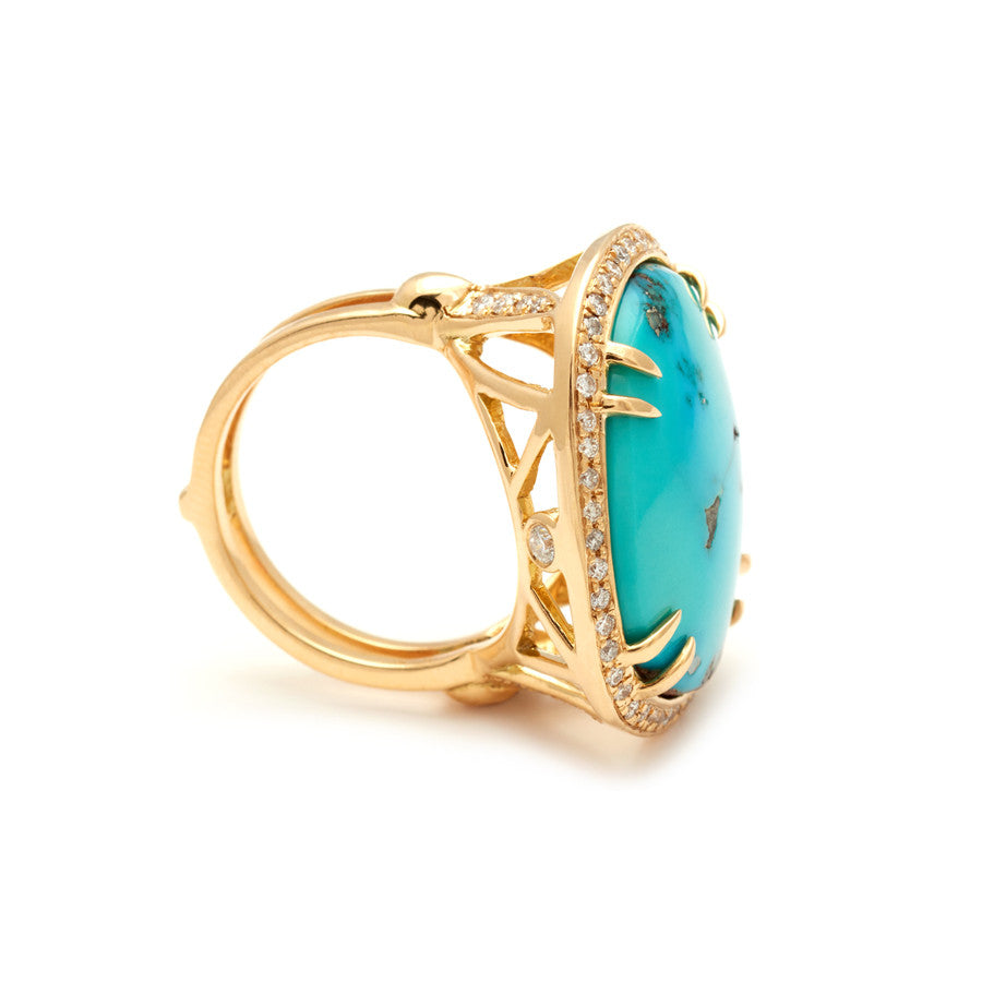 Angled view of an oval shape turquoise center stone with double claw prongs surrounded by a white diamond pave halo set in yellow gold.
