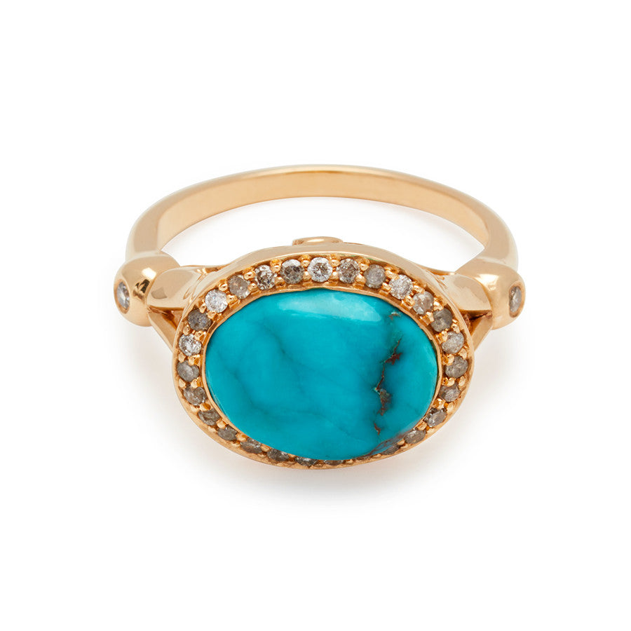 An engagement ring with an oval shape turquoise center stone surrounded by a champagne diamond pave halo with two white diamond accent side stones set in yellow gold.