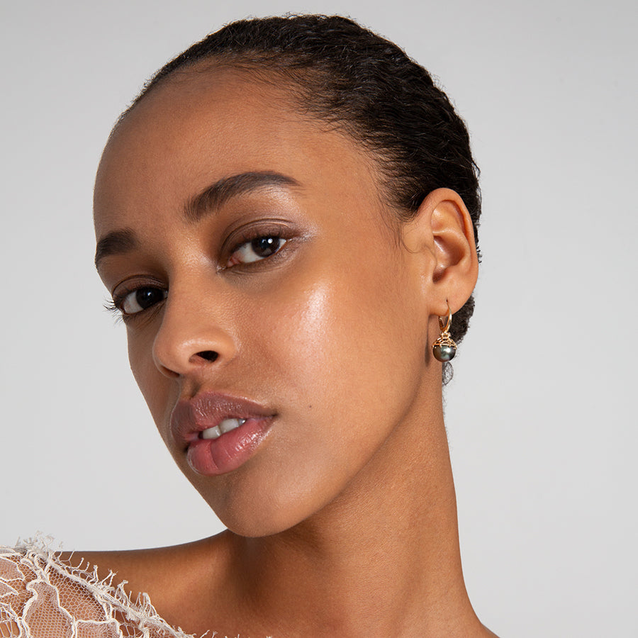 A single hoop with a light pearl hanging from it with grey diamond accents on either side set in yellow gold on a dark-complexion ear - Female wearing Pearl Hoop