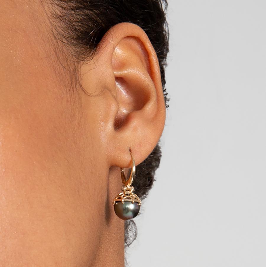 A single hoop with a light pearl hanging from it with grey diamond accents on either side set in yellow gold on a dark-complexion ear - Female Ear wearing the earring
