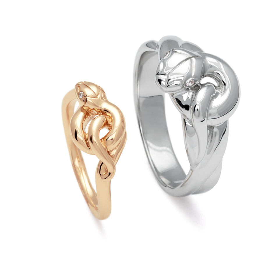 A yellow gold serpent band with white diamond eyes next to a larger white gold serpent band with white diamond eyes.