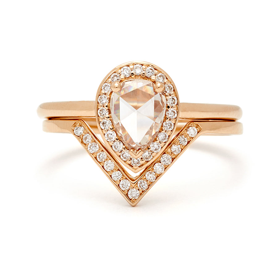 An engagement ring with a pear shape champagne diamond center stone surrounded by a white diamond pave halo set in yellow gold stacked above a white diamond nesting band.
