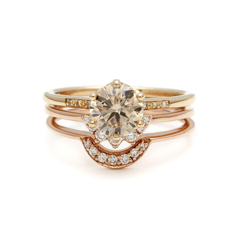 A solitaire ring with a brilliant cut champagne diamond with white diamond pave on either side set in yellow gold stacked above two tiny white diamond curve bands.
