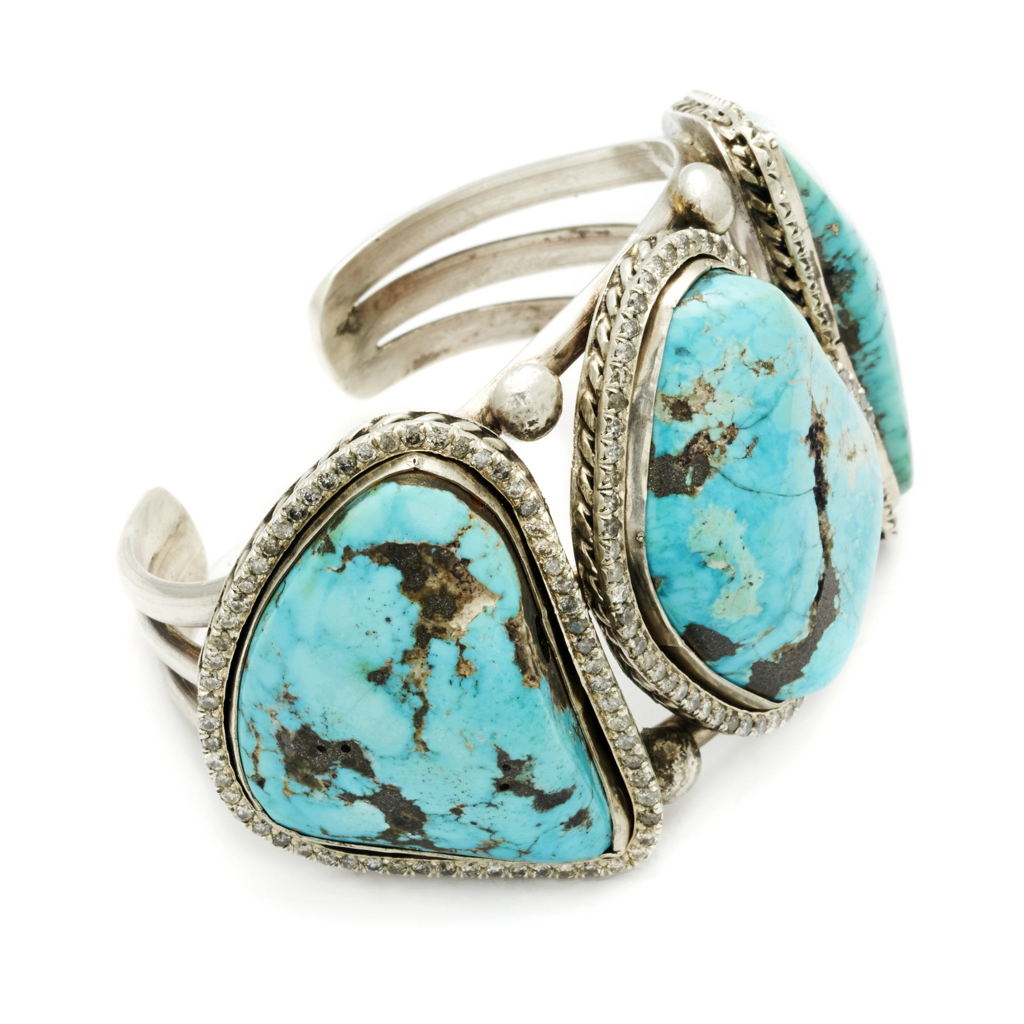 Angled view of a three turquoise stones set in sterling silver with a halo of white diamond set in a cuff.