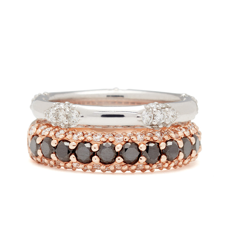 A straight band with 5 clusters white diamond band set in white gold stacked above a band with round black diamonds in a 3/4 pave around a rose gold band with white diamond accents on both top and bottom.