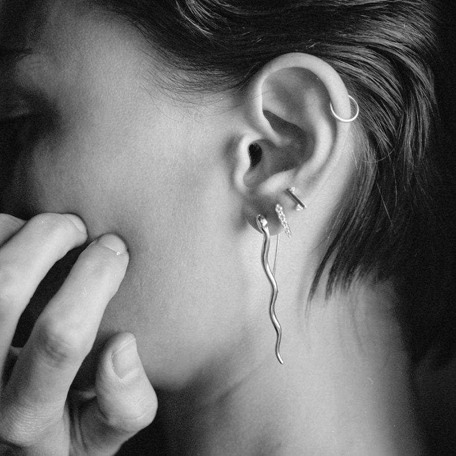 A black and white image of a model with a diamond pointe stud a straight stud and a drop serpent earring.