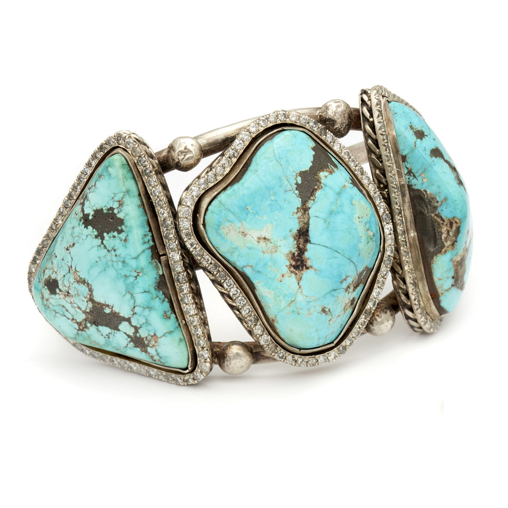 Angled view of a three turquoise stones set in sterling silver with a halo of white diamond set in a cuff.