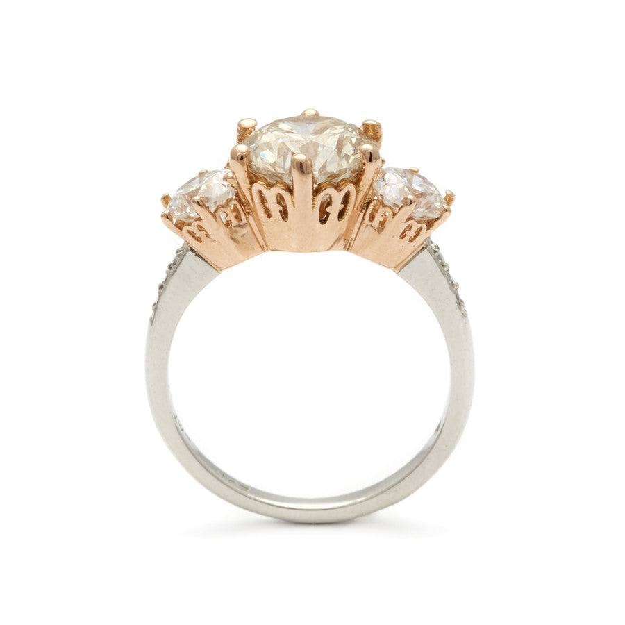 Side view of a three stone engagement ring with a round shape champagne diamond center stone with two white diamond round side stones set in a rose gold basket and a platinum band.