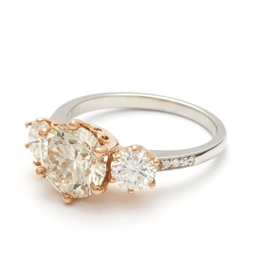 Angled view of a three stone engagement ring with a round shape champagne diamond center stone with two white diamond round side stones set in a rose gold basket and a platinum band.