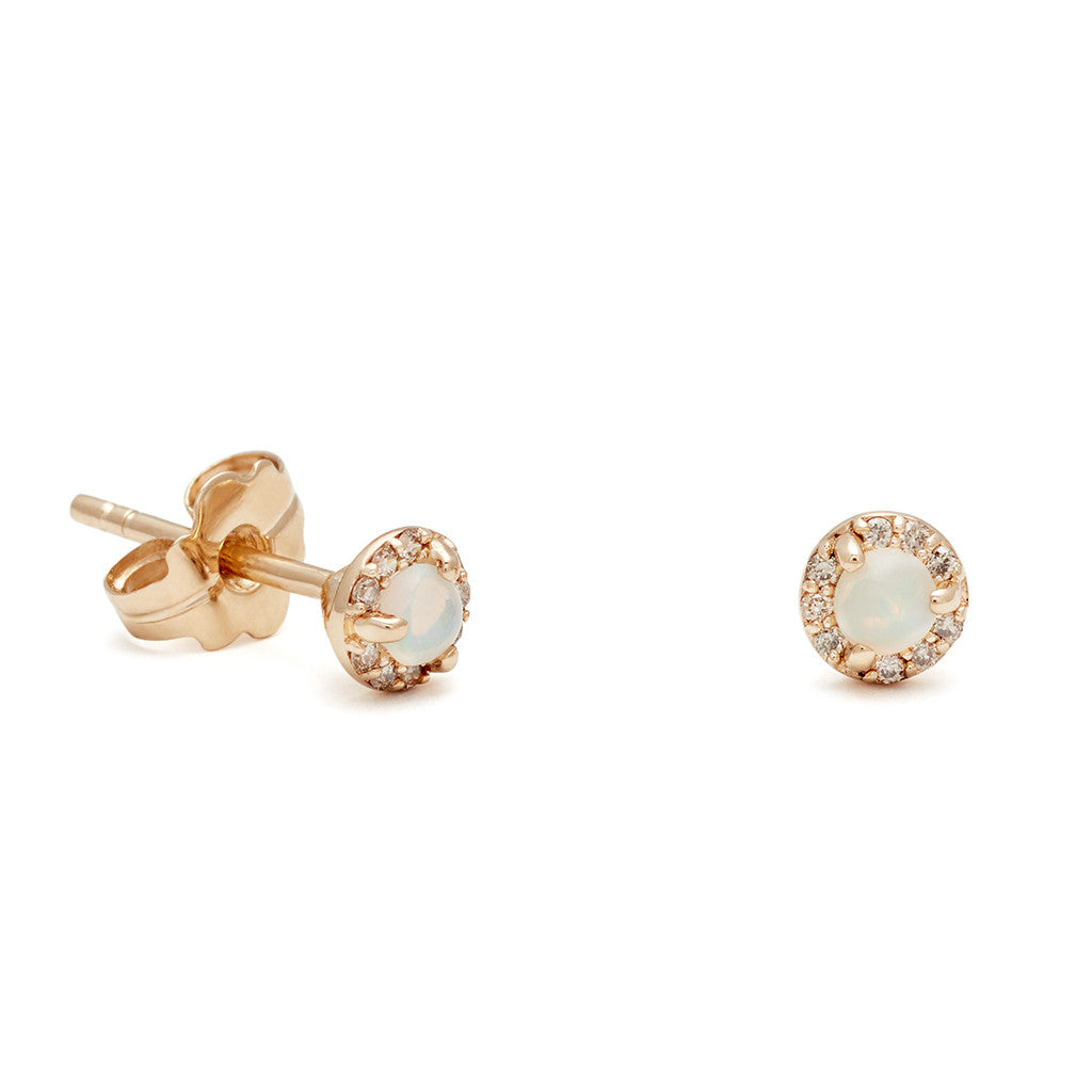 A pair of tiny opal center stone earrings with a halo of champagne diamond set in yellow gold one earring angled.