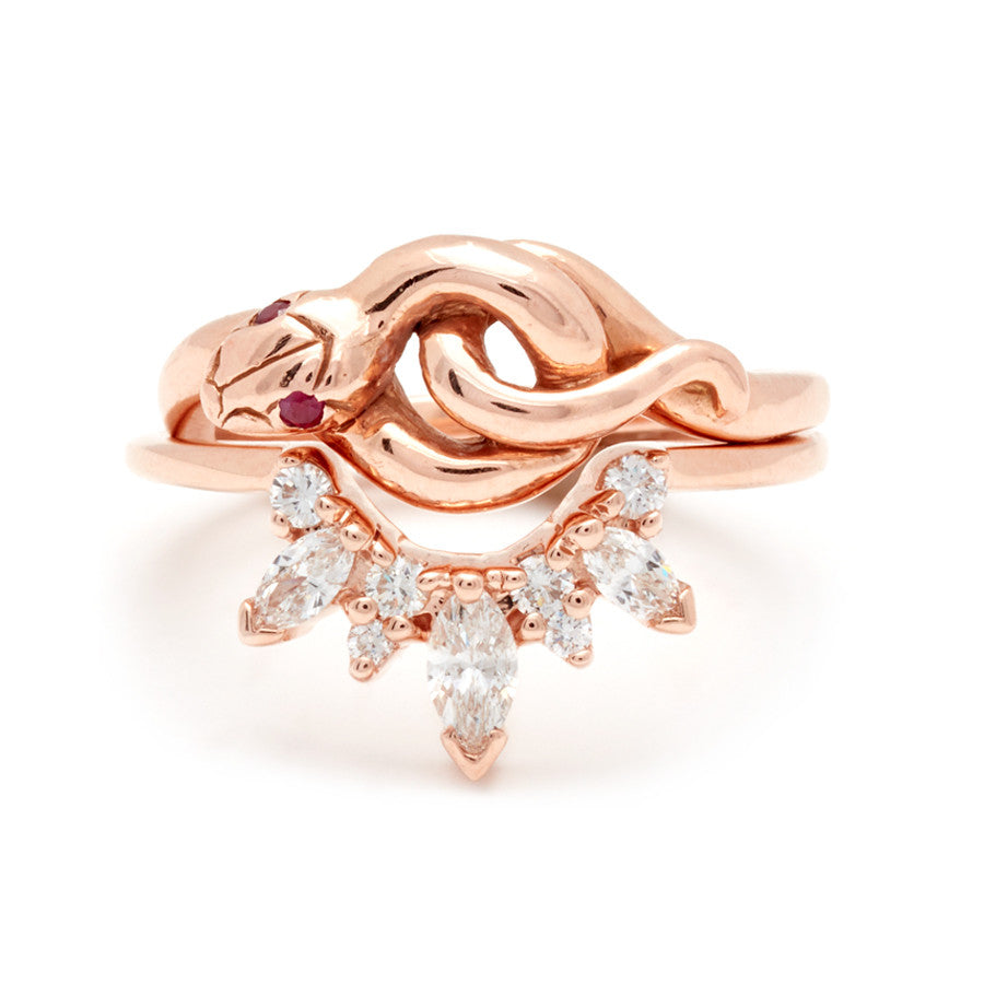 A serpent band with rubies for eyes set in rose gold stacked above a band with marquise and round white diamond stones in rose gold.